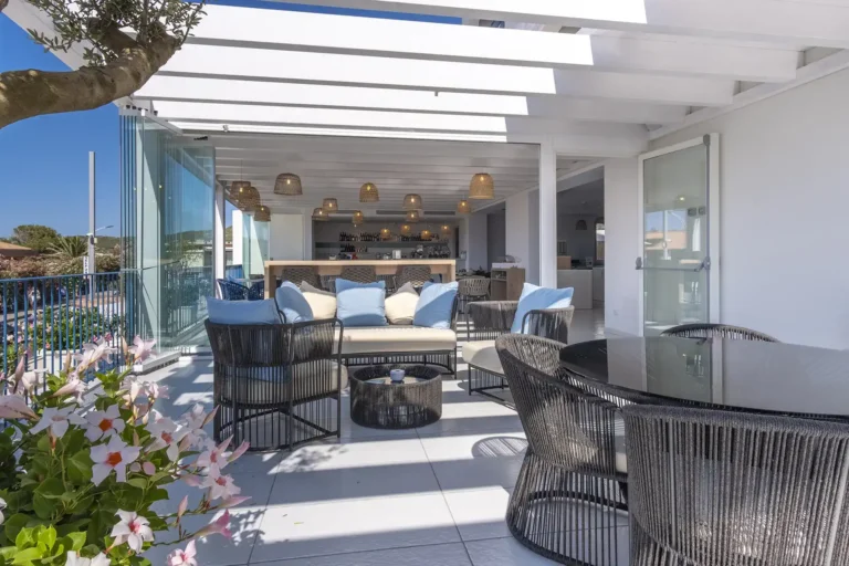 Nell'immagine si vede la terrazza dell'hotel allestita con tavolini, sedie e divanetti dove gli ospiti possono rilassarsi. Sullo sfondo si intravede anche il bancone del bar.